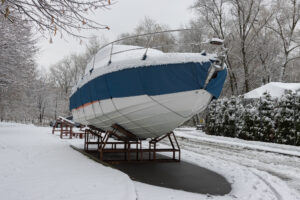 The motorboat is covered with a cover and stands outdoors in the snow. Preparing the boat for winter.